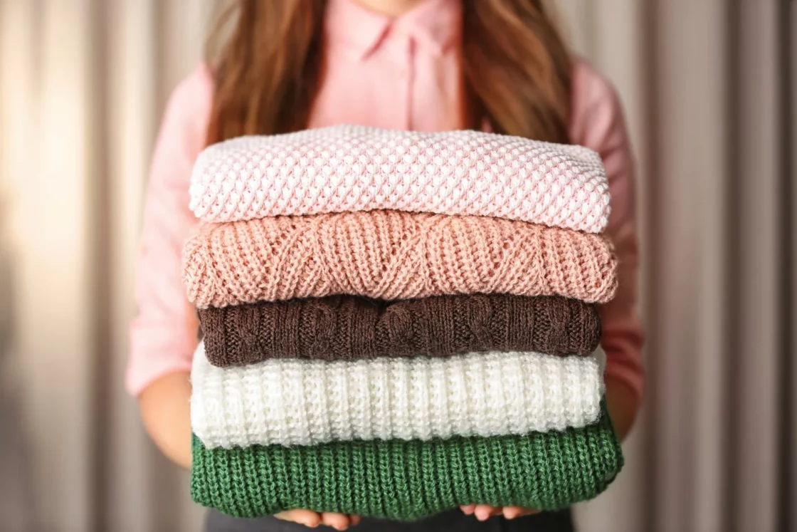 Sweater Care Tips for Spring - woman holding a stack of folded sweaters
